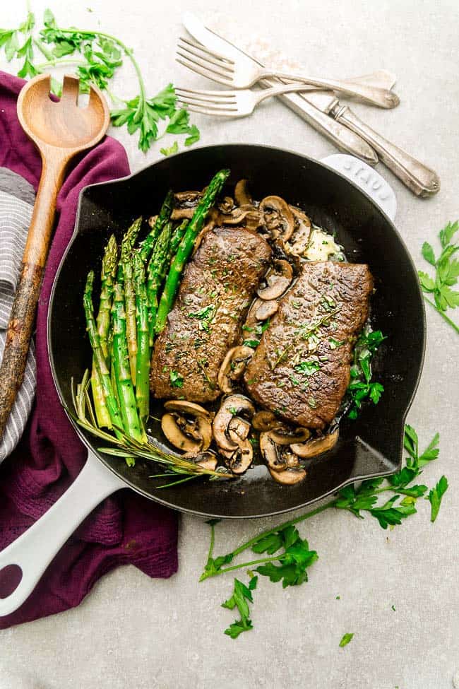 Steak with asparagus, mushrooms, and herbed butter on a cast-iron skillet